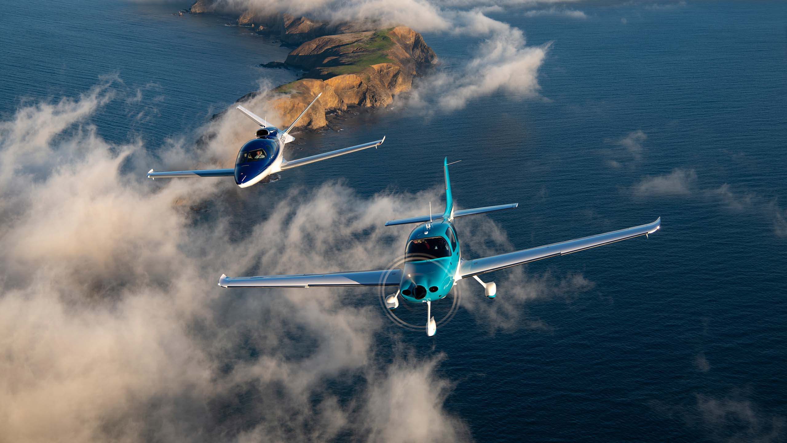 Two Cirrus SR22 aircraft in formation above a coastline